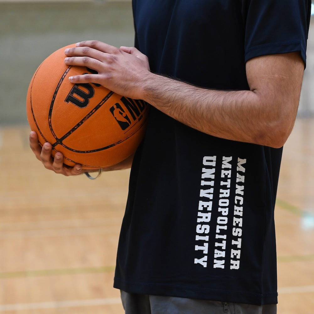 Student holding basket ball wearing black tshirt branded with Manchester Metropolitan University